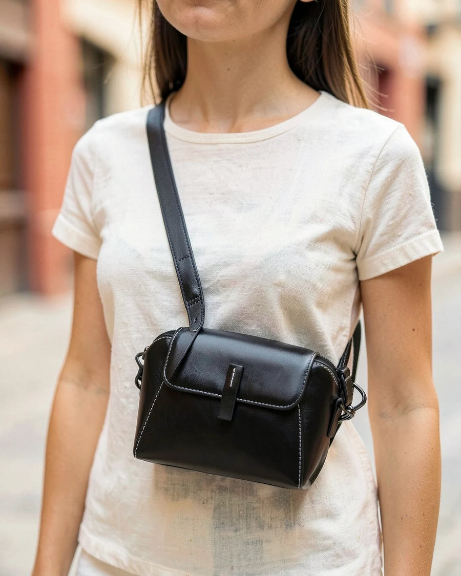 A woman wearing a small black glossy leather crossbody bag at her hip