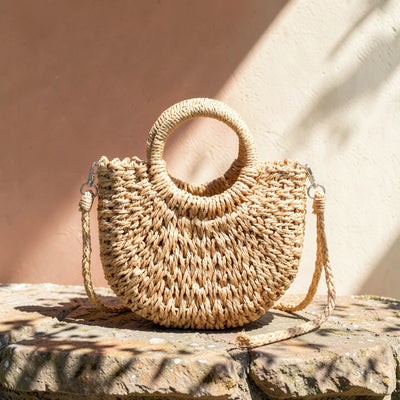 Natural straw woven half-moon crossbody basket bag in sunlight