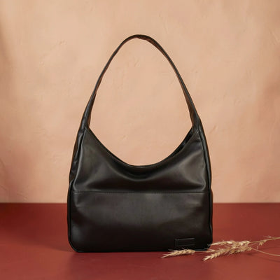 Black smooth leather shoulder bag against a warm plaster backdrop